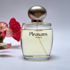 Może przedstawiać: Przezroczysta szklana butelka perfum z srebrną zakrętką. Etykieta zawiera napis "Lauder Pleasures For Men".