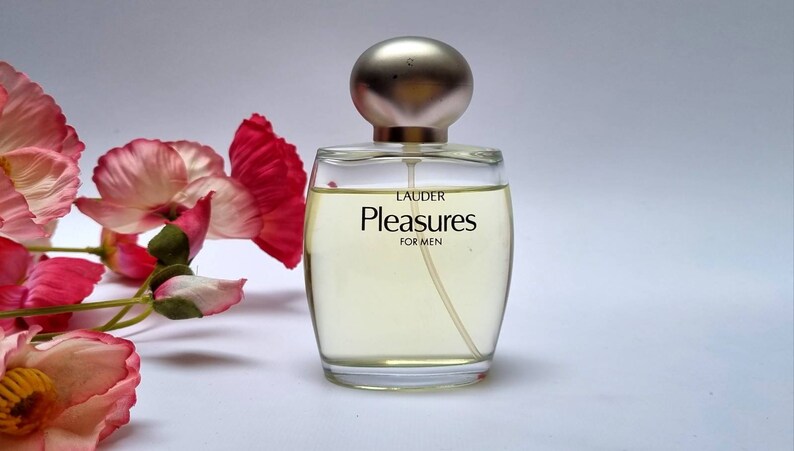 Może przedstawiać: Przezroczysta szklana butelka perfum z srebrną zakrętką. Etykieta zawiera napis "Lauder Pleasures For Men".