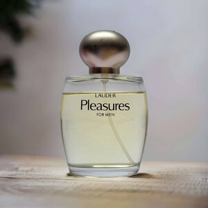 Może przedstawiać: Przezroczysta szklana butelka perfum z srebrną zakrętką. Na etykiecie widnieje napis "LAUDER Pleasures FOR MEN".