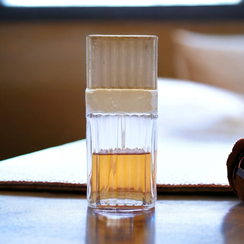 May include: A clear glass bottle with a white cap and a brown liquid inside. The bottle has a textured surface and is sitting on a brown surface.