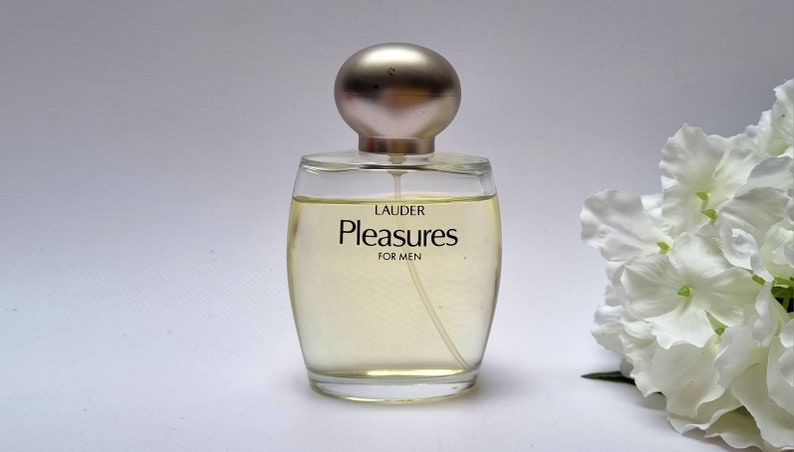 Może przedstawiać: Przezroczysta szklana butelka perfum z srebrną zakrętką. Butelka jest oznaczona etykietą "Lauder Pleasures for Men".