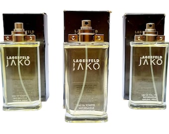 May include: Three glass bottles of Lagerfeld Jako Eau de Toilette Vaporisateur Natural Spray. The bottles are clear and have a gold cap. The bottles are sitting on a white surface.