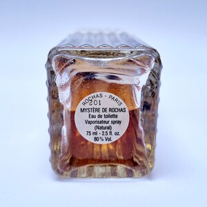 May include: A clear glass bottle of perfume with a brown label that reads "ROCHAS PARIS MYST&Egrave;RE DE ROCHAS Eau de toilette Vaporisateur spray (Natural) 75 ml - 2.5 fl. oz. 80% Vol."