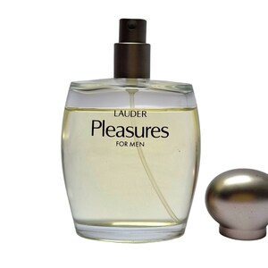 Może przedstawiać: Przezroczysty szklany flakon perfum z złotą zakrętką i srebrnym atomizerem. Etykieta zawiera napis "LAUDER Pleasures FOR MEN".