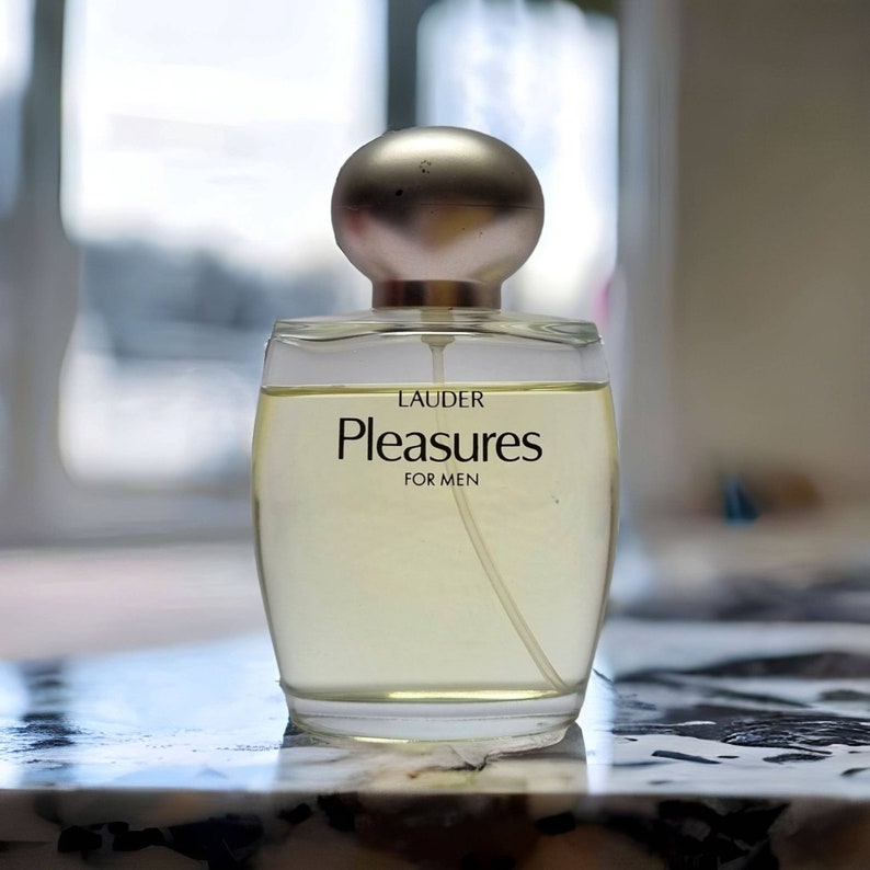 Może przedstawiać: Przezroczysta szklana butelka perfum z złotą zakrętką. Na etykiecie widnieje napis "Lauder Pleasures for Men".