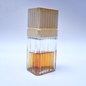 May include: A clear glass bottle with a textured surface and a beige plastic cap. The bottle is filled with a light brown liquid.