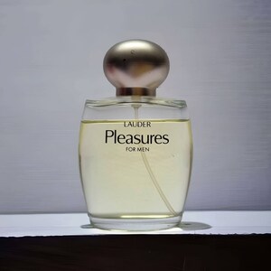 Może przedstawiać: Przezroczysta szklana butelka perfum z srebrną zakrętką. Na etykiecie widnieje napis "LAUDER Pleasures FOR MEN".