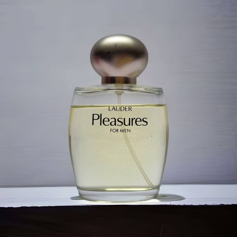 Może przedstawiać: Przezroczysta szklana butelka perfum z srebrną zakrętką. Na etykiecie widnieje napis "LAUDER Pleasures FOR MEN".