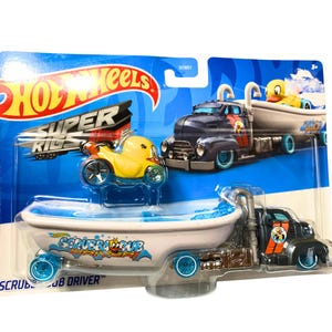 Puede incluir: Conjunto de coches de juguete Hot Wheels Super Rigs con un camión azul y negro con un remolque de bañera blanca. El camión tiene un pato de goma amarillo en la parte delantera y el remolque dice "Scrubber Dub Driver".