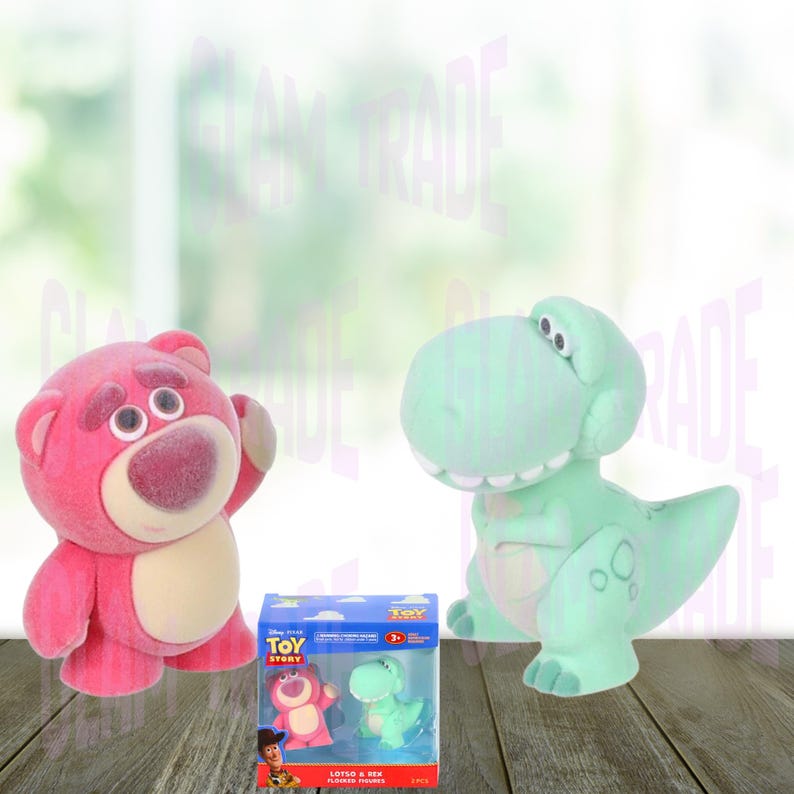 Może przedstawiać: R&oacute;żowy pluszowy miś i zielona zabawka dinozaura z serii Toy Story. Obecny jest r&oacute;wnież mały zestaw pudełkowy tych samych postaci. Zabawki ustawione są na drewnianej powierzchni na rozmytym tle.