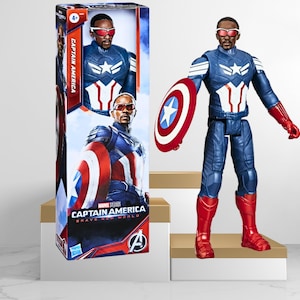 Op de afbeelding: Captain America actionfiguur met een rood, wit en blauw kostuum, die een rood, wit en blauw schild vasthoudt. De figuur staat op een wit platform. De verpakking van de figuur is zichtbaar op de achtergrond.