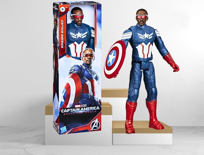 Op de afbeelding: Captain America actionfiguur met een rood, wit en blauw kostuum, die een rood, wit en blauw schild vasthoudt. De figuur staat op een wit platform. De verpakking van de figuur is zichtbaar op de achtergrond.