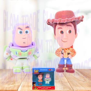Może przedstawiać: Dwie flokowane figurki postaci z Toy Story, Woody i Buzz Lightyear, stoją obok zapakowanego zestawu tych samych postaci. Woody ma na sobie kapelusz kowbojski, koszulę i buty. Buzz Lightyear jest w skafandrze kosmicznym. Na pudełku napis "Woody & Buzz Lightyear Flocked Figures".