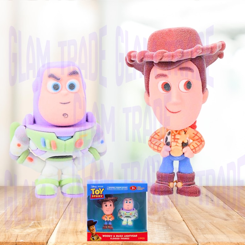 Może przedstawiać: Dwie flokowane figurki postaci z Toy Story, Woody i Buzz Lightyear, stoją obok zapakowanego zestawu tych samych postaci. Woody ma na sobie kapelusz kowbojski, koszulę i buty. Buzz Lightyear jest w skafandrze kosmicznym. Na pudełku napis "Woody & Buzz Lightyear Flocked Figures".