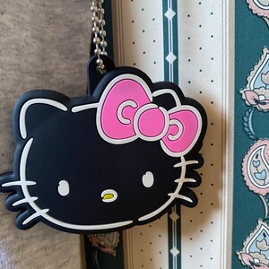 May include: Black and white Hello Kitty charm with a pink bow. The charm is attached to a silver chain.