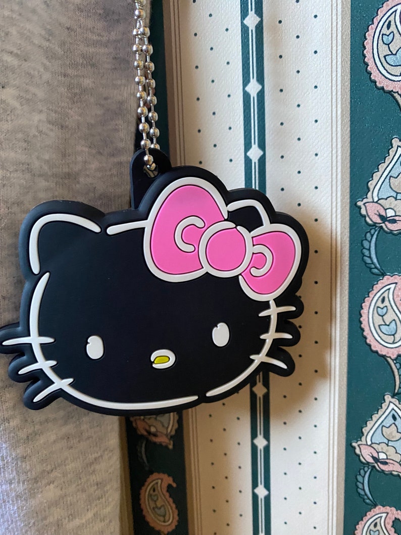May include: Black and white Hello Kitty charm with a pink bow. The charm is attached to a silver chain.