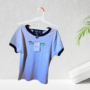 May include: Gray short-sleeved t-shirt with a black and white ringer neckline. The shirt features a graphic of four cartoon characters with the text "Forever 21" on the front.