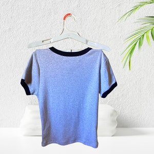 May include: A gray short-sleeved t-shirt with a black trim around the neckline and sleeves. The shirt is hanging on a white hanger.