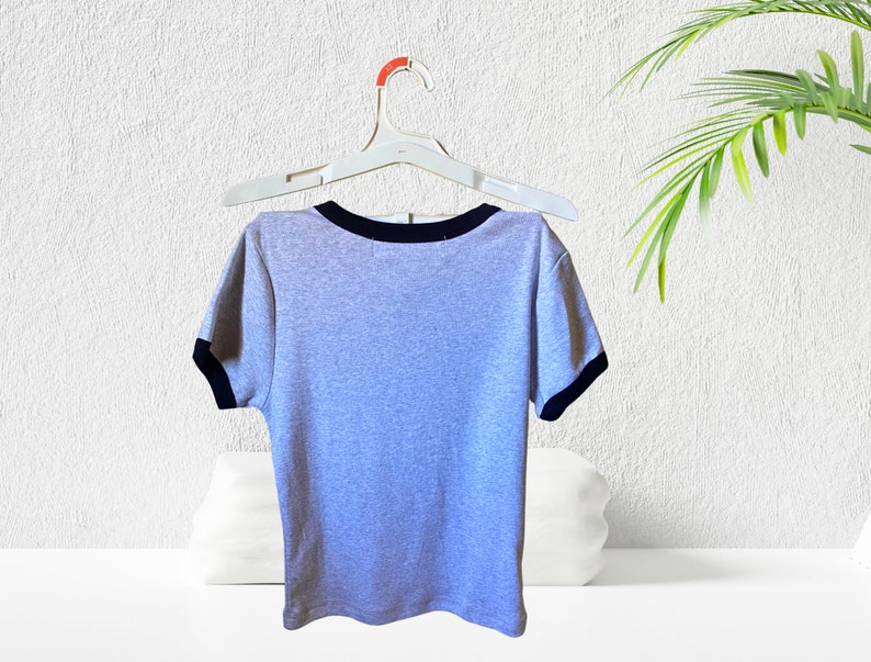 May include: A gray short-sleeved t-shirt with a black trim around the neckline and sleeves. The shirt is hanging on a white hanger.