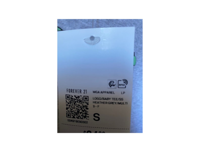May include: A white tag with black text and a barcode. The tag reads "FOREVER 21 WGA APPAREL LP LOGO/BABY TEE/SS HEATHER GREY/MULTI 9-F S 004919090302"