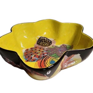 Könnte beinhalten: Eine blumenförmige Keramikschale mit leuchtend gelbem Innenraum und dunkelbrauner Außenseite. Die Innenseite zeigt ein buntes abstraktes Muster mit roten, orangefarbenen und schwarzen kreisförmigen und organischen Formen auf der gelben Fläche.