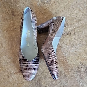 Può includere: Un paio di scarpe col tacco alto marrone e bronzo. Le scarpe hanno un aspetto strutturato, simile a quello di un rettile. Il nome del marchio "pizzio" è visibile sulla soletta di una scarpa. I tacchi sono alti circa 7,6 cm.