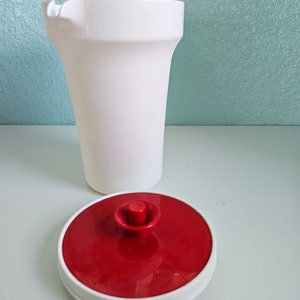 Può includere: Brocca bianca con coperchio rosso e un pomo bianco in cima. La brocca è in plastica e ha un beccuccio per versare.