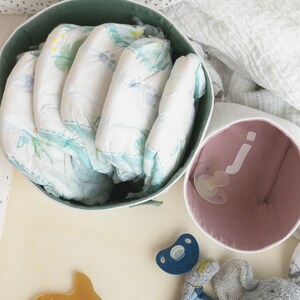 Lifestyle photo of two white fabric boxes from above. The bigger one on the left has pastel green inside - diapers are inside. The smaller one on the right has pastel rose inside and white letter j and a pacifier is inside.