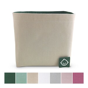 Puede incluir: Un contenedor de almacenamiento de lona beige con una parte superior verde y una pequeña etiqueta verde con una cara sonriente blanca. El contenedor se muestra sobre un fondo blanco. La imagen también incluye una fila de muestras de color: verde oscuro, verde claro, beige, blanco, gris, rosa y rojo.