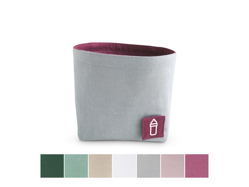 Front view of grey fabric storage basket with mulberry pink inside and square label with white clipart of milk bottle. Underneath seven squares with fabric colours: dark green, pastel green, beige, white, light grey, pastel rose and mulberry pink.