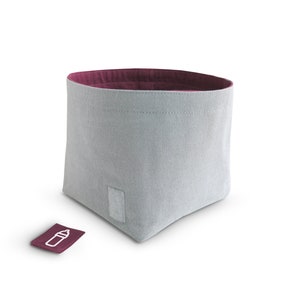 Front view of grey fabric storage bin with mulberry pink inside and grey rectangle hook-and-loop fastener on the front side. The mulberry pink square label with white clipart of milk bottle lays infront of the basket.