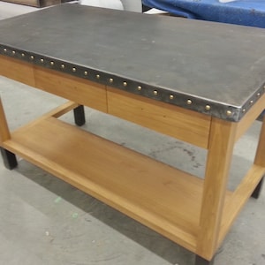 May include: A wooden table with a metal top and two drawers. The table has a shelf underneath and black legs.