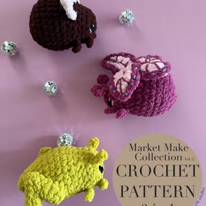 May include: Three crocheted creatures in shades of brown, purple, and yellow are displayed against a pink background. The creatures have large eyes and are accompanied by small disco balls. The image also includes text that reads "Market Make Collection Vol. 2 CROCHET PATTERN 3 in 1."