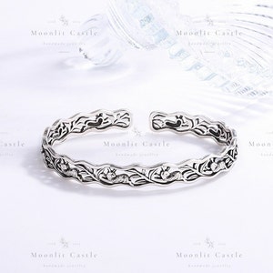 May include: An open-ended silver cuff bracelet featuring a repeating embossed pattern of small rabbits nestled among leafy vines. The metal has an oxidised finish to highlight the intricate details of the wildlife and foliage motifs along the band.