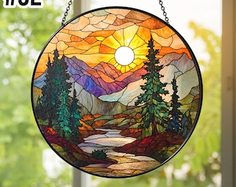 May include: A circular stained glass suncatcher featuring a landscape scene with a bright white sun, orange sky, purple and blue mountains, green pine trees, and a flowing river. The piece is framed in black metal and hangs from a chain. Text #S2.