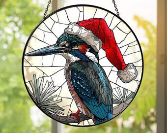 May include: Stained glass window art featuring a colorful kingfisher bird wearing a red Santa hat. The bird is perched on a branch, set against a white background with a black circular frame and hanging chain. The artwork is designed for window display.