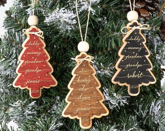 May include: Three Christmas tree-shaped wooden ornaments in red, brown, and black. Each ornament features a layered design with white script names, small star cutouts, a twine string with a wooden bead, and the year 2024 engraved at the base.