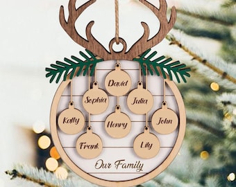 May include: A circular wooden Christmas ornament featuring a brown deer antler top and green pine branch accents. The center displays the text Our Family and seven smaller circular wooden tags engraved with the names David, Sophia, Julia, Katty, Henry, John, Frank, and Lily.
