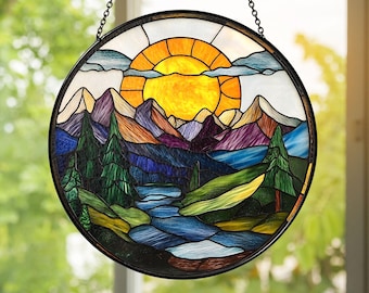 May include: A round stained glass panel depicting a mountain landscape with a bright yellow sun, blue river, and colorful mountains. The panel is framed in black and hangs from a chain.