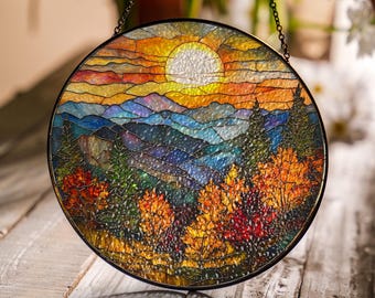 May include: A round stained glass panel depicting a sunset over a mountain range. The sun is a bright white circle, and the sky is a gradient of orange, yellow, and blue. The mountains are shades of blue and purple, and the trees are green and orange.