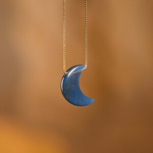 May include: A gold chain necklace with a blue crescent moon pendant.