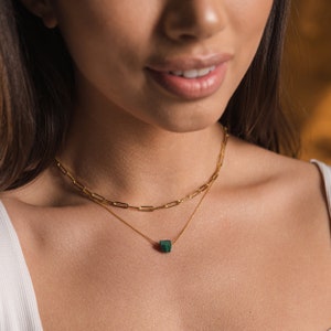 May include: A gold chain necklace with a green gemstone pendant. The necklace is layered with a second, thinner chain.