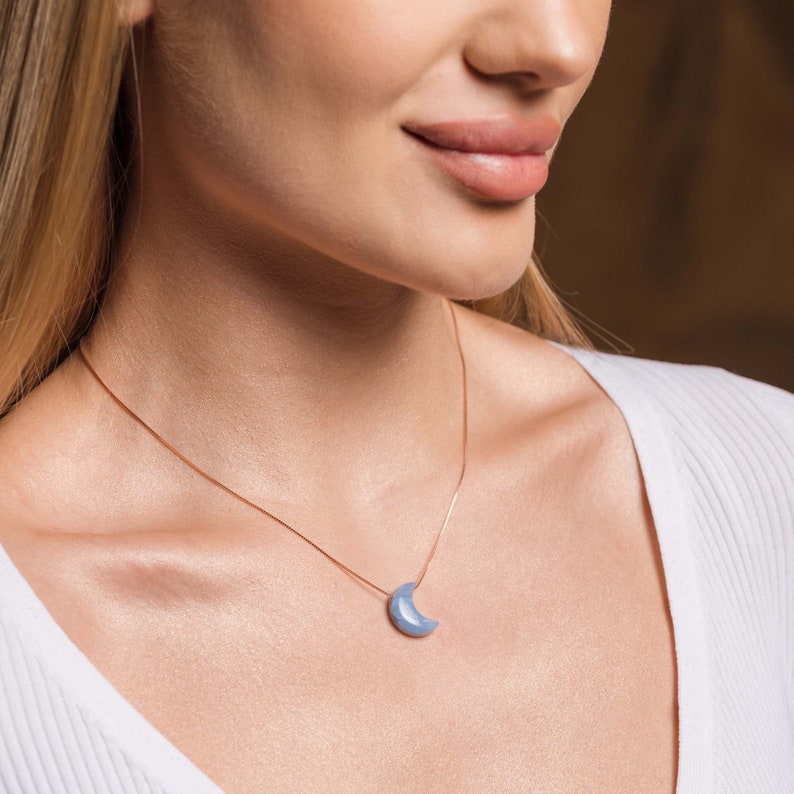 May include: A delicate silver chain necklace with a light blue crescent moon pendant.