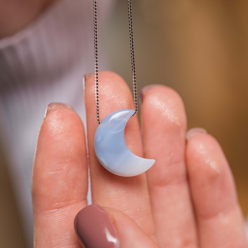 May include: A silver chain necklace with a light blue crescent moon pendant.