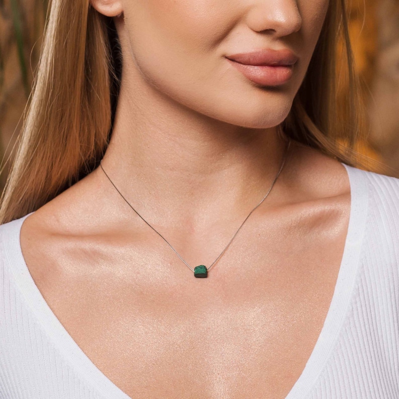May include: A silver chain necklace with a small, dark green malachite stone pendant.