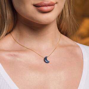May include: A gold chain necklace with a crescent moon pendant made of blue gemstone.