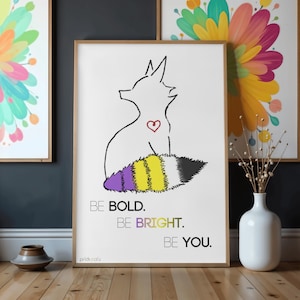 May include: A framed art print featuring a line drawing of a fox-like creature with a heart and a non-binary pride flag tail. The text "BE BOLD. BE BRIGHT. BE YOU." is below the image. The artwork is displayed on a wooden floor.