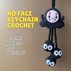 Könnte beinhalten: Ein handgefertigter schwarzer Häkel-Schlüsselanhänger mit dem No-Face-Charakter aus Spirited Away. Der Schlüsselanhänger hat ein weißes Gesicht mit roten Markierungen und drei herabhängenden Rußmännchen mit weißen Augen. Der Text auf dem Bild lautet "NO FACE KEYCHAIN CROCHET".