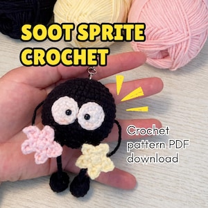 May include: A handmade black Soot Sprite crochet keychain with white eyes and star-shaped arms in pink and yellow. The text "SOOT SPRITE CROCHET" is displayed above the keychain, with "Crochet pattern PDF download" below.