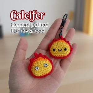 May include: Two crocheted Calcifer keychains. The keychains are yellow with red flames and black eyes and mouth. The text "Calcifer Crochet pattern PDF download" is in the upper left corner.